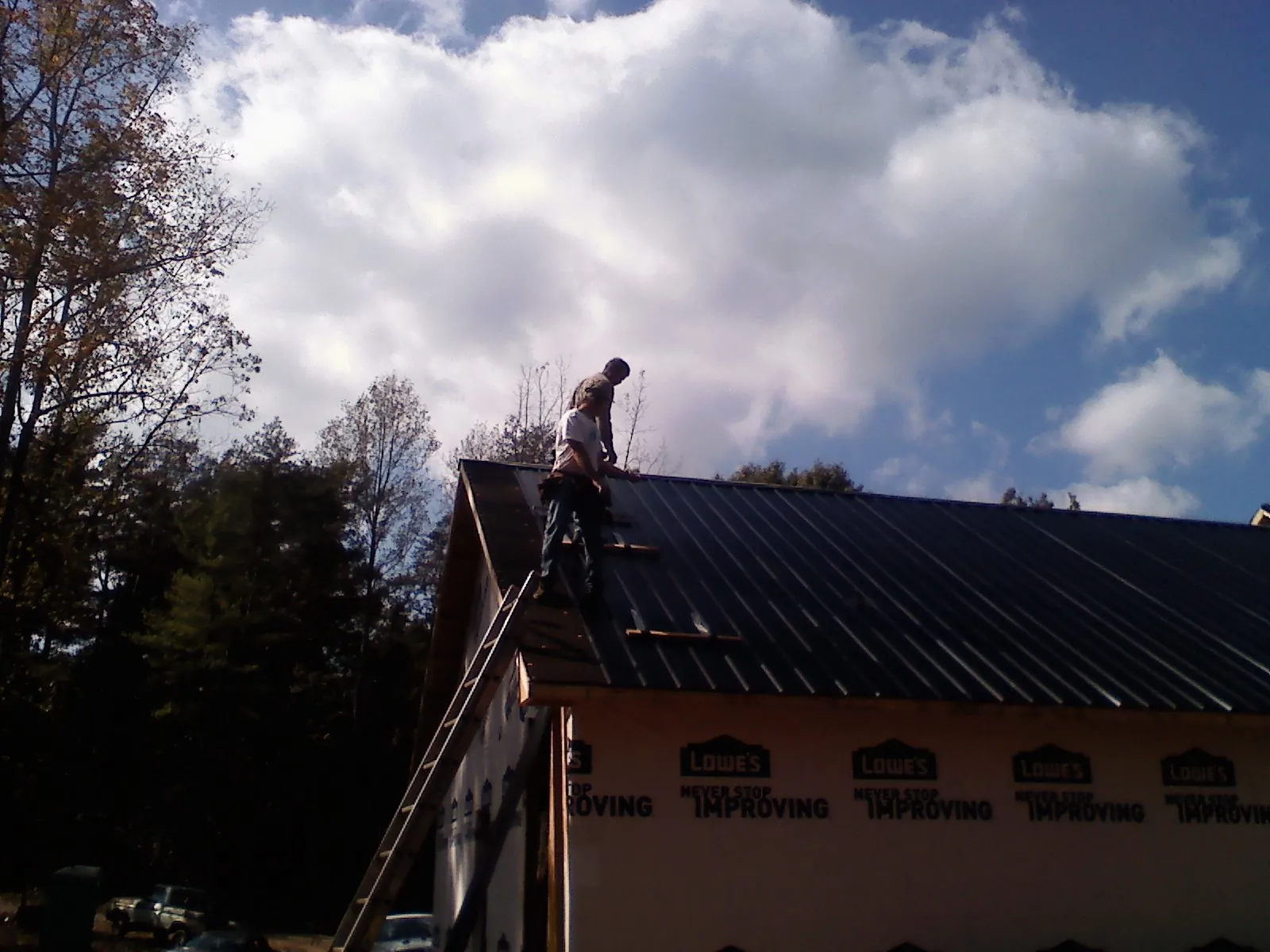 Roofer fastening dark metal panels high against a cloudy sky, from a Roof Inspection job in Gray